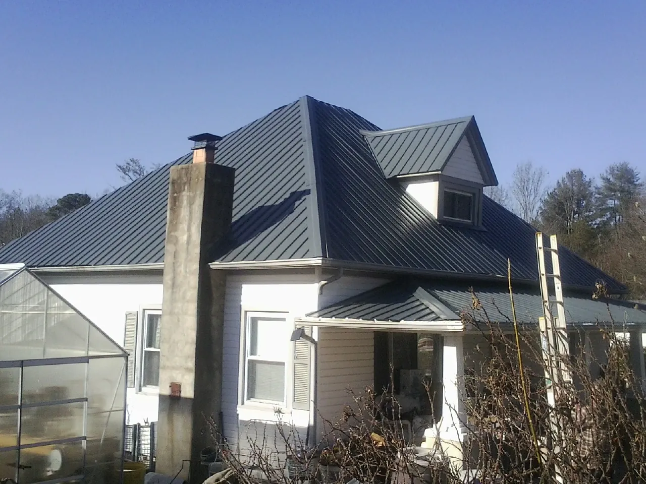 Dark blue standing seam metal roof on a white farmhouse with dormer — Slate & Tile Roof Repair by Roofing Brothers in Archer