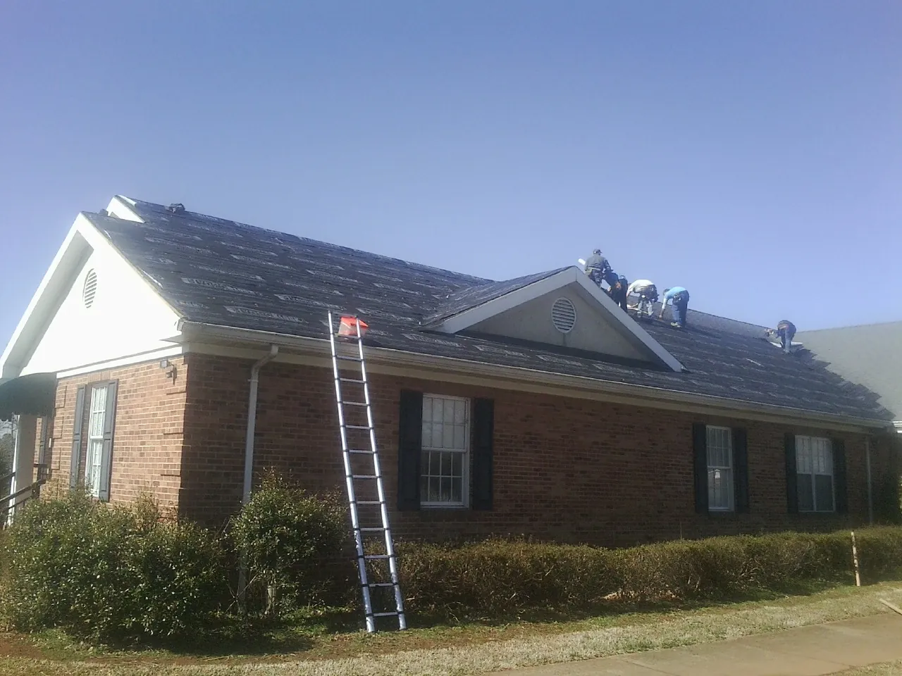 Crew tearing shingles off a brick ranch roof with a ladder set — Emergency Roof Repair work by our crew in Archer