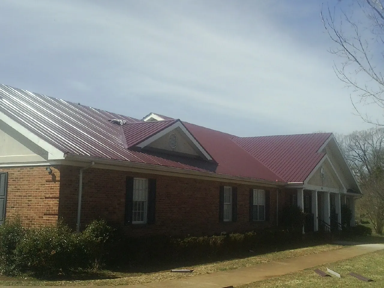 Red metal roof with gabled entries on a long brick building, from a Hail Damage Roof Repair job in Archer