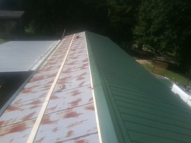 Old rusted panels beside newly installed green metal roofing — Wind Damage Roof Repair by Roofing Brothers in Archer