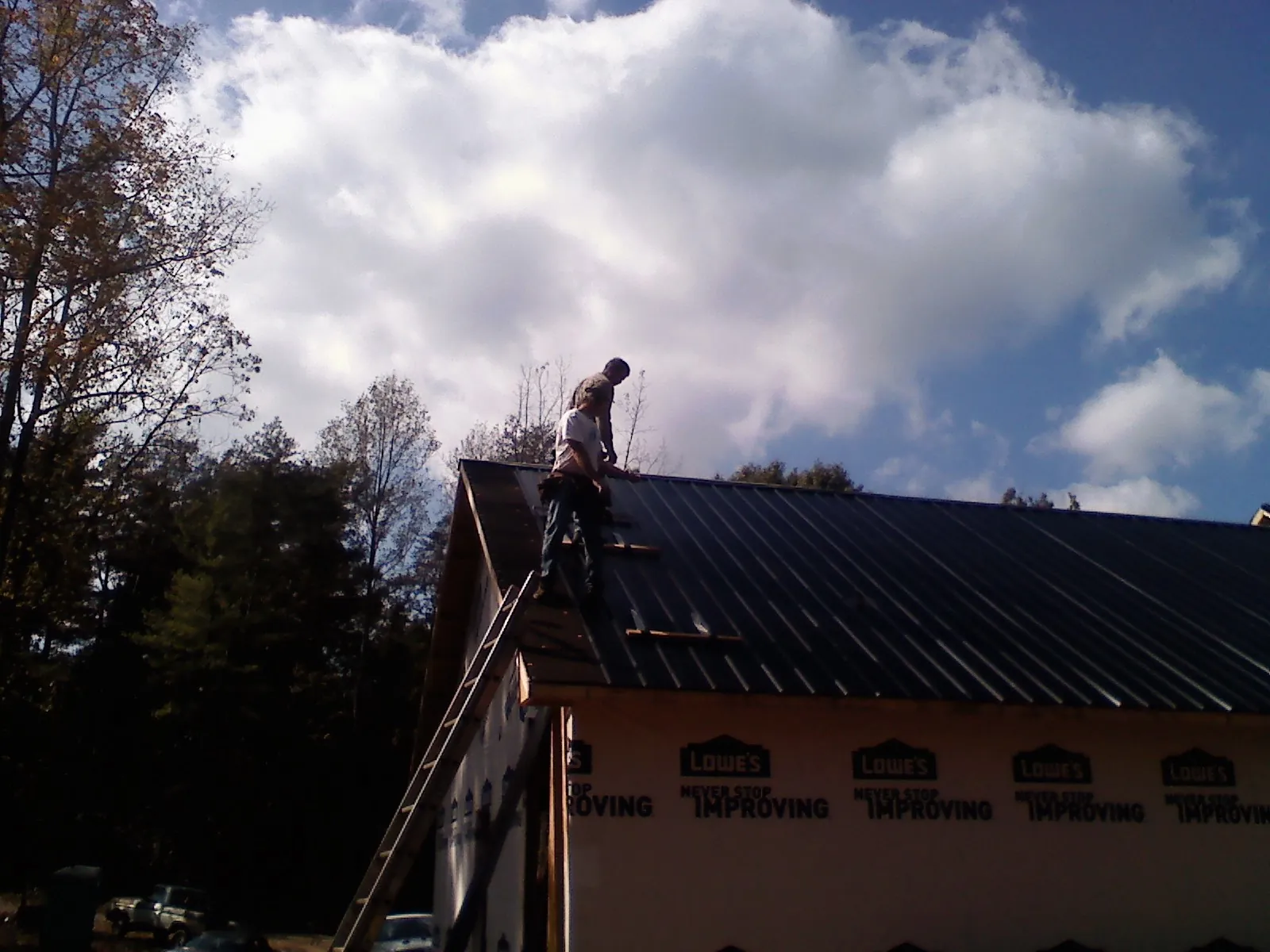 Roofer fastening dark metal panels high against a cloudy sky, from a Roof Inspection job in Archer