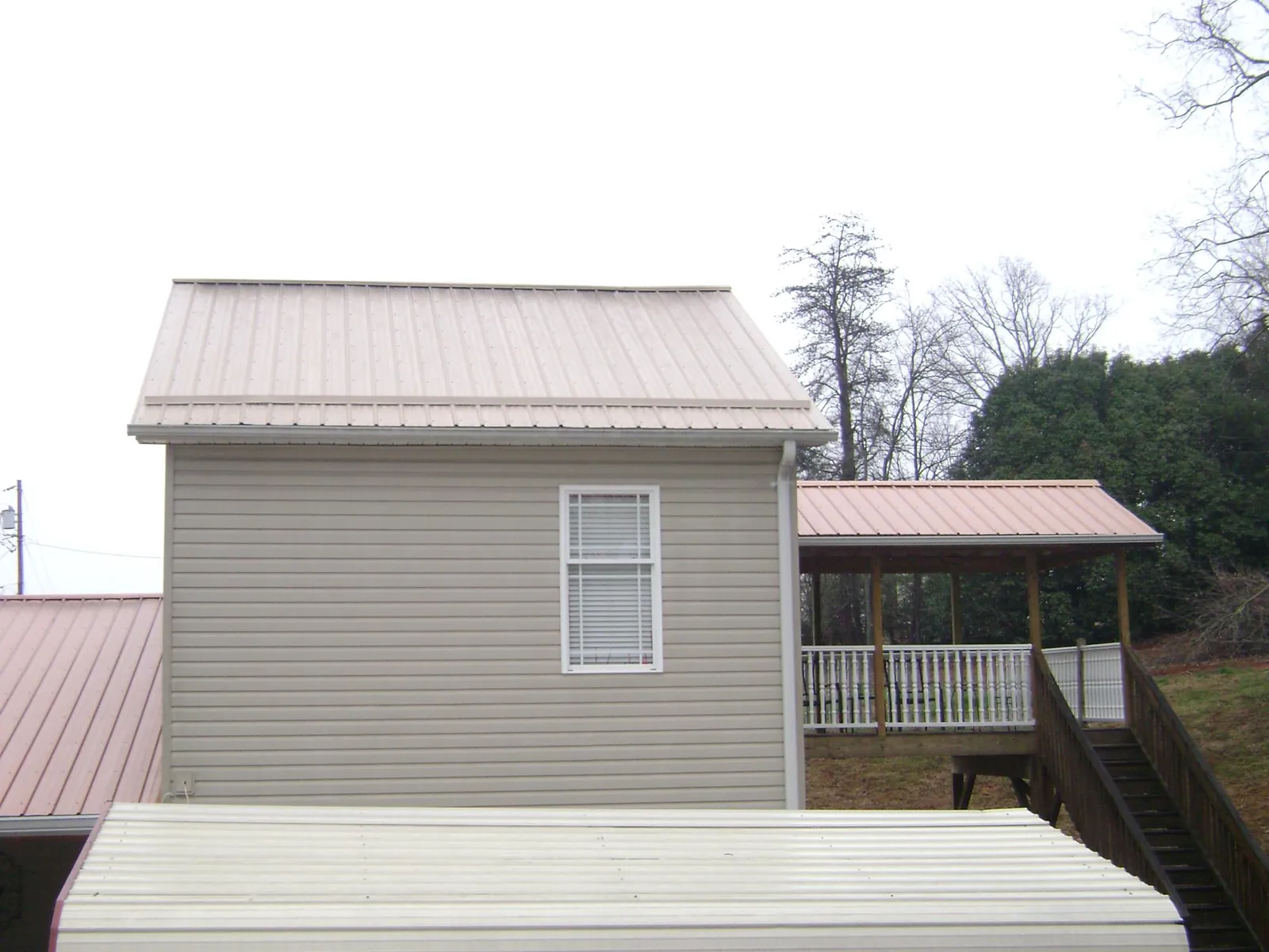 Tan metal roofs on a two story addition and attached porch, from a Roof Replacement job in Archer