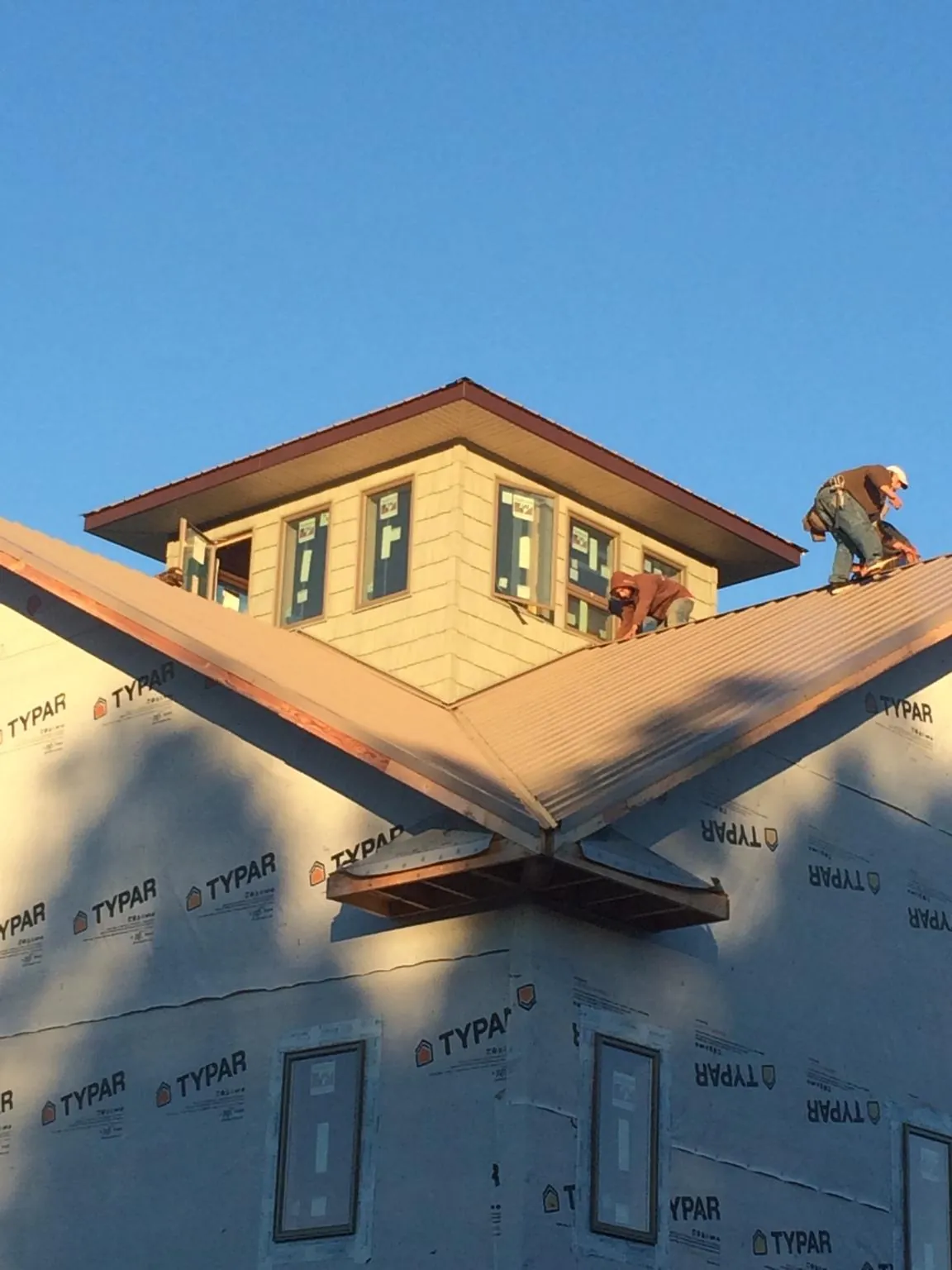 Roofers working around a rooftop cupola on a new metal roof at sunset — Roof Waterproofing in Archer by Roofing Brothers